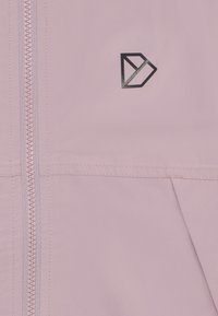 Rosa softshell-jakke med lynlås, stikninger og et sort geometrisk logo på venstre side. Letvægts med en glat tekstur.