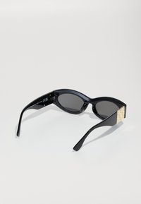 Black sunglasses with oval lenses, glossy frame, and textured gold-accented temple. Dark tinted lenses provide contrast against the frame.