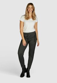 Jogging noir texturé avec taille élastique et poches zippées sur les côtés, associé à un t-shirt blanc ajusté et des bottines noires.