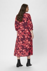 Robe midi d'un bordeaux profond avec un motif floral dans des teintes de rose. Dotée de manches ballons et d'une silhouette fluide. Des bottines noires à la cheville complètent le look.