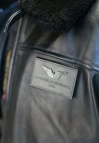 Veste en cuir noir avec col en shearling. Comprend un écusson avec un emblème d'aigle et le texte "Patrouille de France 1953".