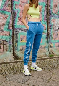Blue sweatpants with white drawstring and logo, paired with a lime green crop top and white Nike sneakers with black accents.