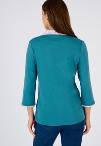 Tee lange mouwen top in teal met een bloemenpatroon op de kraag en manchetten. Glad materiaal met een ontspannen pasvorm, voorzien van een gebogen zoom en driekwartmouwen.