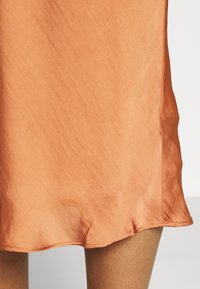 Satinová sukně na slip v teplé oranžové barvě. Vyznačuje se volným střihem s mírně volánkovým lemem a hladkým povrchem.