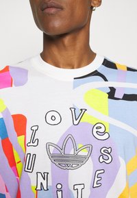 Flerfärgad grafisk t-shirt i bomull med livliga virvlar av rosa, blått och gult. Har texten "KÄRLEK" och "ENAD", samt en logotypdetalj.