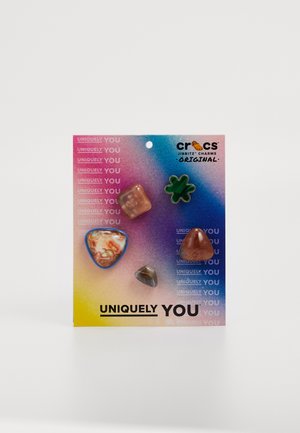 Ensemble de cinq charms Jibbitz de Crocs représentant différentes formes : un cœur, un trèfle et trois pierres précieuses dans des nuances d'orange et de vert sur un fond dégradé.