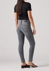 Jeans skinny de tiro alto en gris con dos bolsillos traseros y un ligero desvanecimiento. Combinados con una camiseta ajustada negra y sandalias negras de tacón block.
