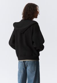 Felpa nera con cappuccio e vestibilità comoda, abbinata a jeans di denim azzurro chiaro. La felpa presenta un orlo a coste e una texture morbida.