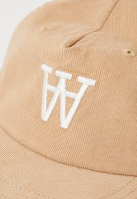 Svijetlosmeđi kapica od kordura s bijelim izvezenim "W" logotipom; sadrži teksturirani materijal i šivane detalje za poboljšanu izdržljivost.