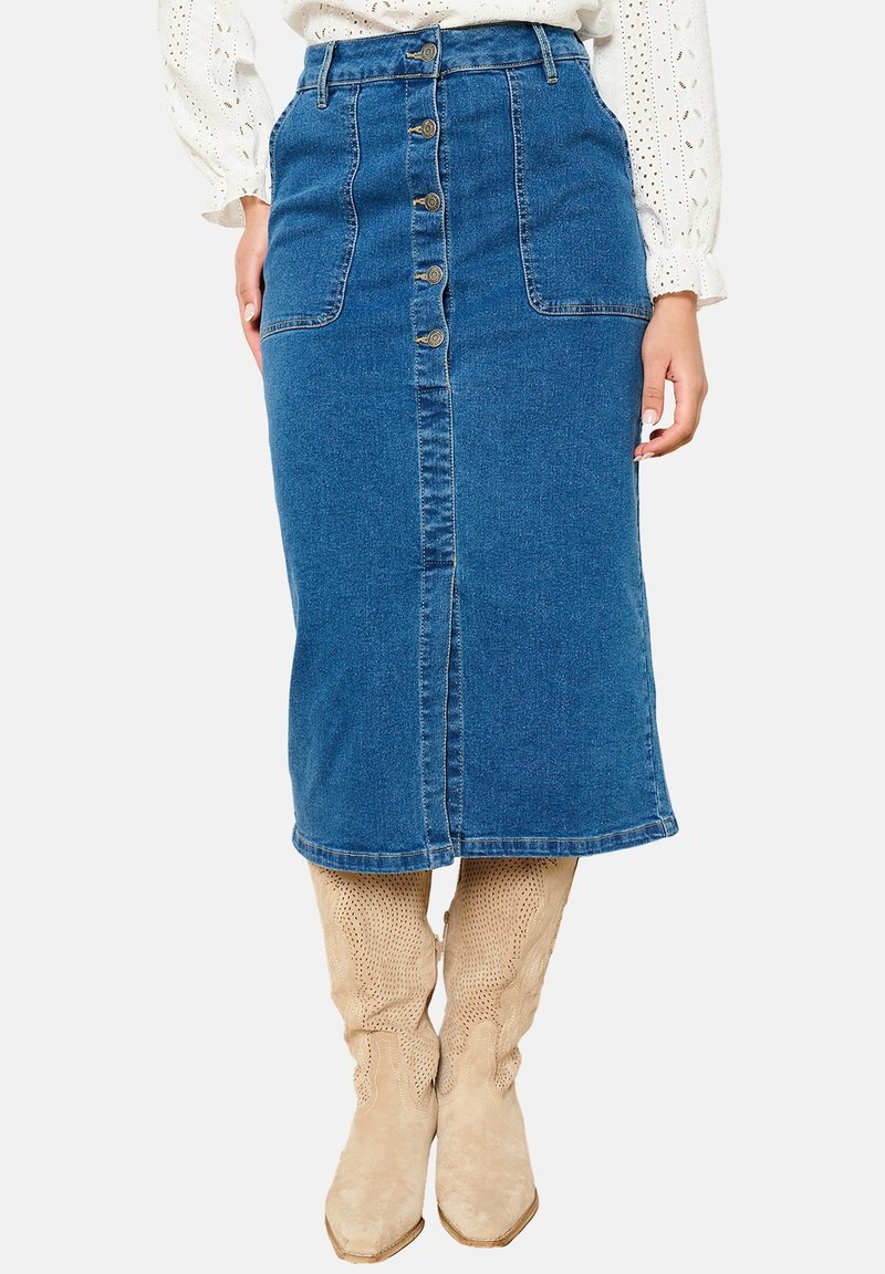 Jeans mini krilo z zapiranjem na gumb spredaj, dvema sprednjima žepoma, do kolen, v srednje modri barvi; v kombinaciji s svetlo bež škornji do kolen.