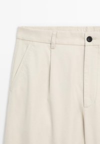 Beige trousers with a smooth cotton fabric, featuring a flat front, side pockets, a belt loop, and a black button closure at the waist.