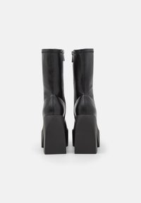 Zwarte leren hoge hakken laarzen met een slank ontwerp, vierkant plateau en zichtbare stiksels. Voorzien van een ritssluiting aan de achterkant.