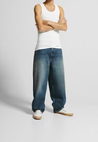 Vit ribbad linne, lösa ljusblå denimjeans med en urtvättad look, och vita sneakers med krämfärgade gummisulor.