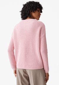 Maglione rosa a maglia con una texture a costine, spalle scese e una vestibilità morbida, abbinato a pantaloni beige.