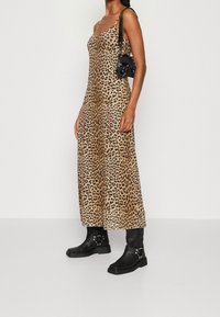 Leopardmönstrad, ärmlös maxiklänning i nyanser av beige och brunt, ihop med svarta ankelskor och en liten svart crossbody-väska.