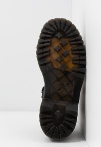 Černá gumová podrážka boty s hlubokými drážkami, s diamantovými vzory a zesílenou patou. Ukazuje texturovaný povrch pro lepší přilnavost.