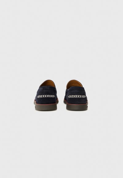 Tengerészkék velúr slip-on cipők sima felülettel, fehér láncvarrás részlettel és kontrasztos piros gumitalppal.