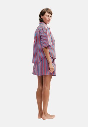 Femme debout pieds nus portant une chemise ample à manches courtes à rayures verticales multicolores et un short assorti, regardant par-dessus son épaule.