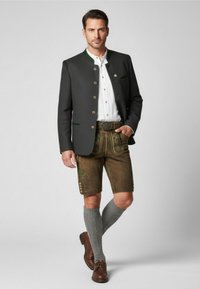 Traditionele mannenoutfit met een donkere jas met groene accenten, een wit shirt, bruine leren shorts met groene borduursels en grijze sokken.