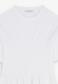 White dress with short sleeves. Features gathered smocking at the waist, flowing skirt, and soft, smooth fabric texture. Brand label visible.