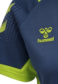 Marineblauwe sportshirt met gele accenten, gemaakt van ademend meshmateriaal. Heeft een gestructureerd oppervlak en een prominent Hummel-logo.