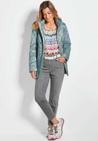 Helle türkisfarbene Daunenjacke, gemustertes, mehrfarbiges Shirt darunter, graue Hose und bunte Sneaker. Strukturierter Stoff und lässige Passform.