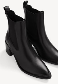 Černé kožené kotníkové boty s elastickými bočními panely, špičatými špičkami a blokovým podpatkem. Hladký povrch s minimálními detaily šití.