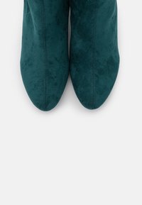 Ein Paar türkisfarbene Wildleder-Stiefel mit spitzem Zehenbereich, von oben auf einem weißen Hintergrund fotografiert.