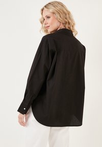 Black long-sleeve shirt with a relaxed fit, buttoned cuffs, and a curved hem. Made from lightweight fabric with a smooth texture.