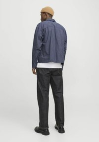 Tjekket navy skjorte med en afslappet pasform, parret med mørke denimjeans. Har lange ærmer, en klassisk krave og runde sorte sko.