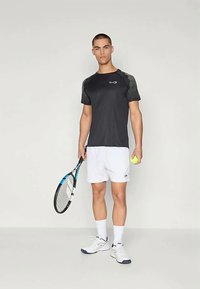 Camiseta atlética negra de manga corta con detalles de malla, pantalones cortos blancos, raqueta de tenis y pelota, con un diseño moderno y tejido ligero.