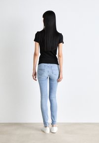 Top negro de manga corta y jeans ajustados de color azul claro. Los jeans tienen un diseño de cinco bolsillos. Un par de zapatos blancos sin cordones completan el conjunto.