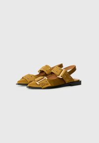 Slingback sandale od žute nubuk kože, s dva podesiva remena sa zlatnim detaljima i uskim nosom na ravnom crnom đonu.