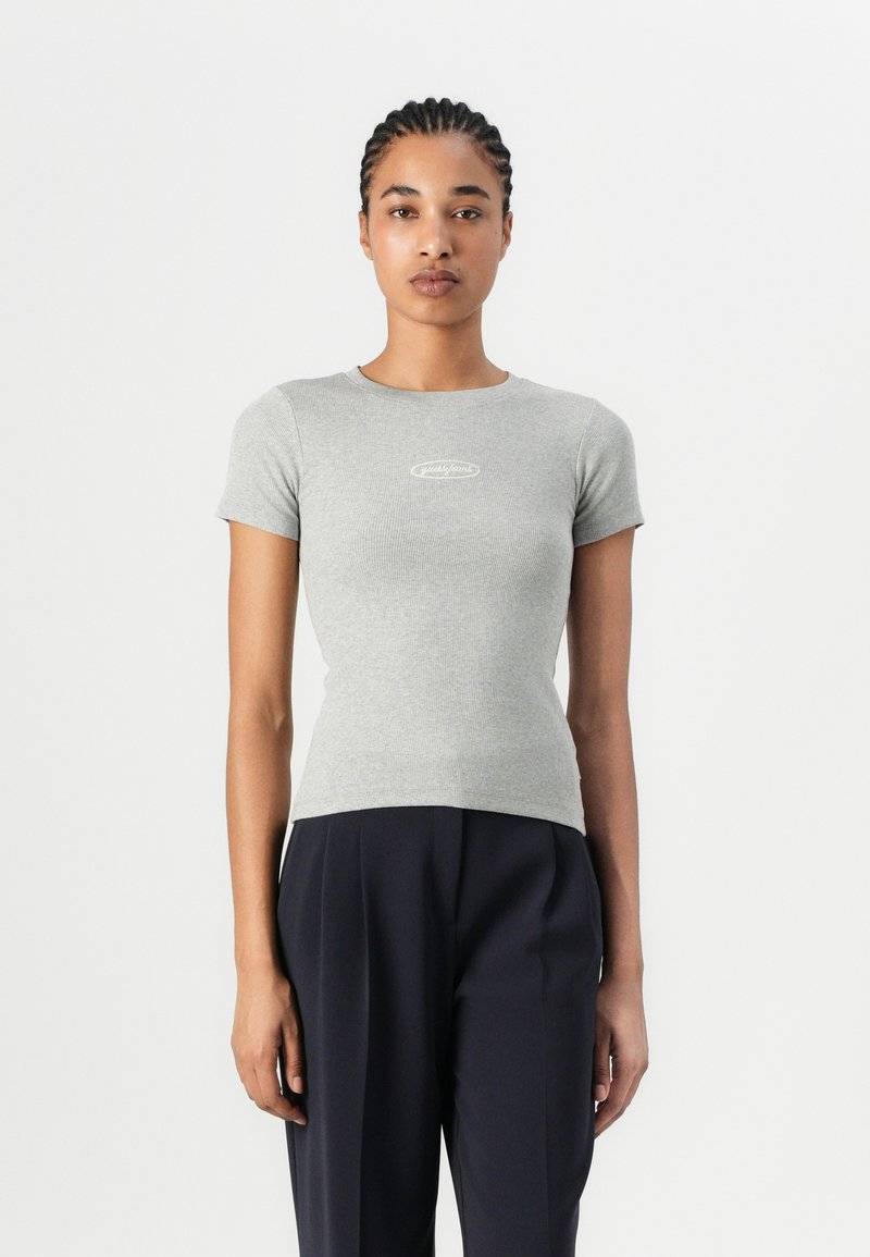 T-shirt grigio a maniche corte con righe, dal design aderente e un piccolo logo bianco sul petto, abbinato a pantaloni scuri larghi.