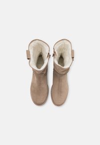 Paire de bottes d'hiver en daim beige avec doublure polaire blanche douce, visible vue de dessus sur un fond clair uni.