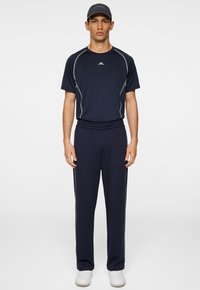 Marinblå sportoutfit som består av en kortärmad skjorta med ljusgrå accenter och byxor med elastisk midja; kompletterad med en matchande keps.