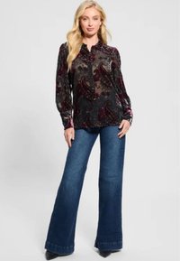 Blusa a motif paisley nera e borgogna con maniche lunghe e chiusura a bottoni, abbinata a jeans in denim scuri a zampa d'elefante e scarpe nere a punta.