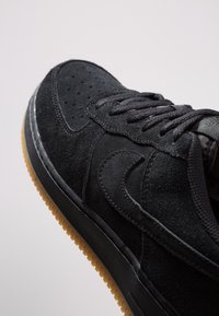 Sneaker in camoscio nero con punta perforata, lacci piatti neri, suola in gomma e suola in gomma contrastante. Presenta un design elegante con accenti cuciti.