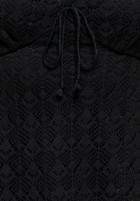 Tissu en crochet noir avec motifs en losange et en éventail, doté d'un lien tressé avec des franges au centre supérieur.