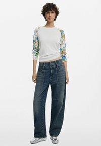 Maglione bianco con maniche a fantasia floreale, abbinato a jeans blu scuro a vita alta e dal taglio morbido con grandi tasche. Sneakers argentate.