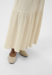Beige tiered fabric skirt with textured weave, paired with beige mules featuring a pointed toe and flat sole.