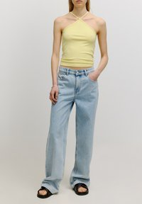 Lichtgele ribbed haltertop met kruislijfbanden, gecombineerd met hoog-waisted lichtblauwe wijde denim jeans en zwarte sandalen.