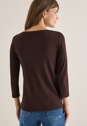 Brun langærmet top i en blød, glat stof, med bådhals og tætsiddende design, parret med blå denim jeans.