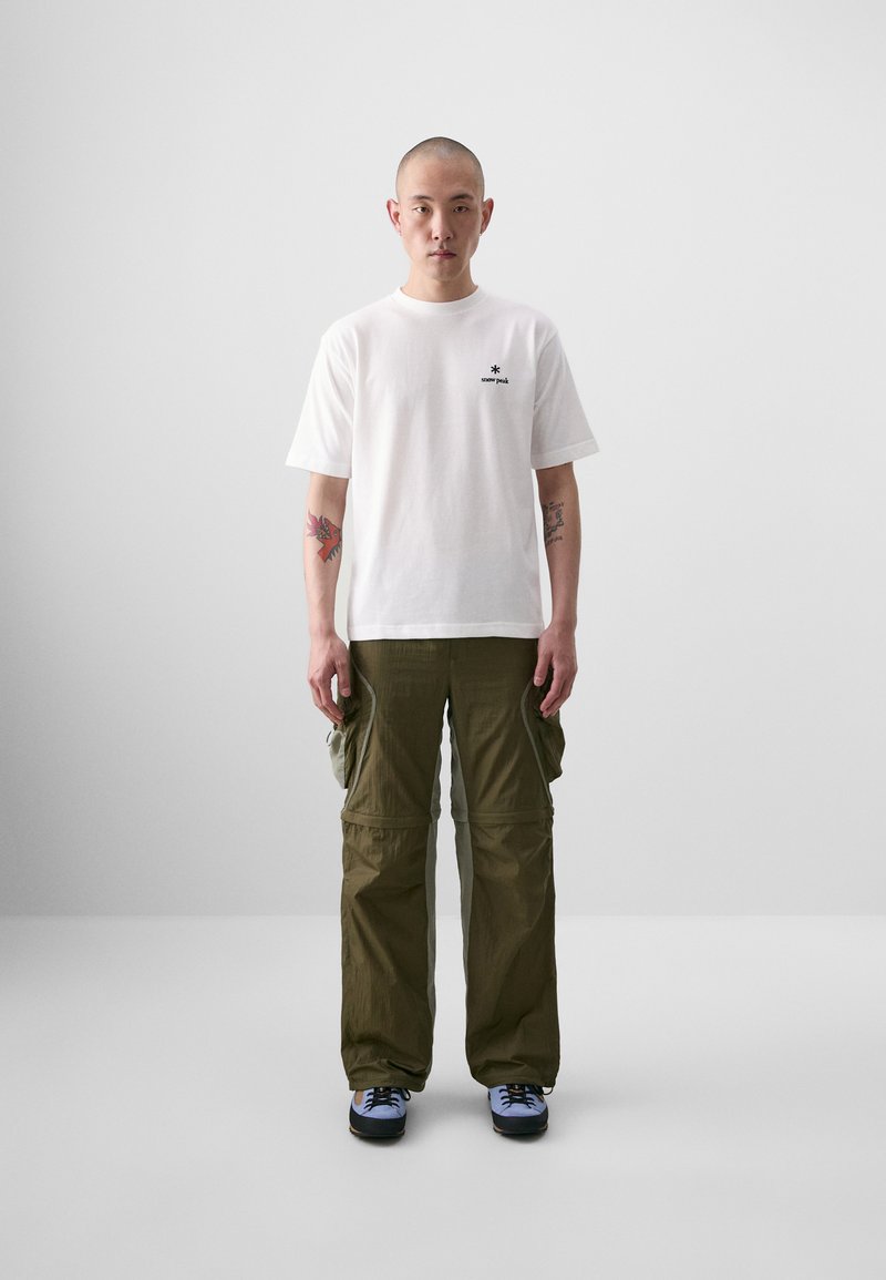 T-shirt en coton blanc avec un petit logo noir sur la poitrine, associé à un pantalon cargo vert olive avec plusieurs poches et un fit décontracté.