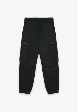 Pantaloni cargo neri in tessuto intrecciato, con cinturino elasticizzato, coulisse e due tasche laterali con cerniera. Polsini elasticizzati alle caviglie.