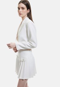 Witte blazer met lange mouwen en een diepe V-hals, gecombineerd met een geplooide witte minirok met kleine zakken. Glad stoftextrue.