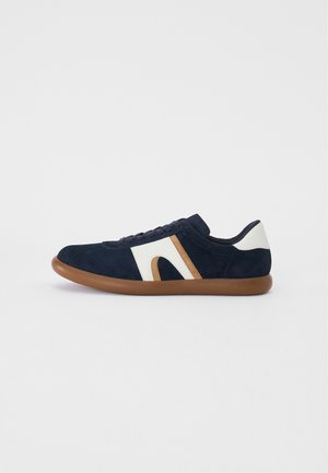 Navy suede sneaker with light cream and tan accents, round toe, low profile, rubber outsole, and lacing system on the upper.