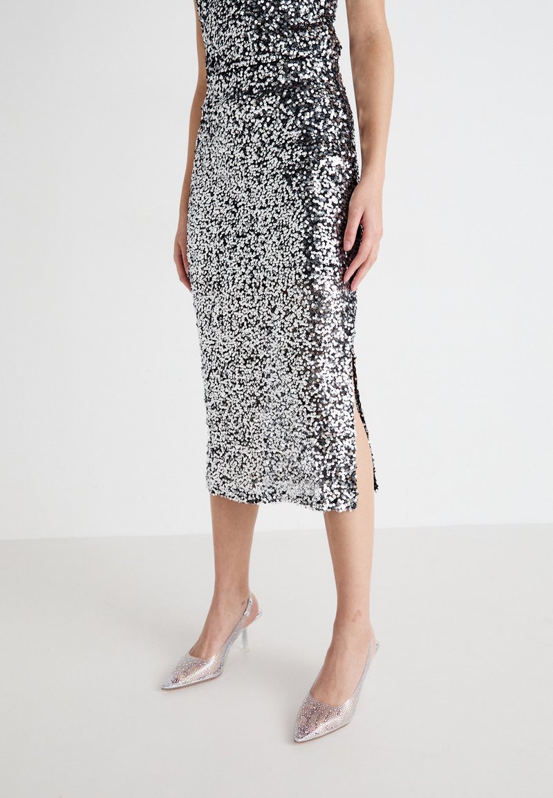 Blej z midi dolžino s sijočimi tkaninami in oprijetim silhueto; srebrna in črna barva, stranski razporek, s sijočo teksturo. V kombinaciji s srebrnimi čevlji z visokimi petami v obliki konice.