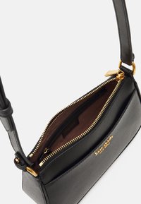 Sac à main en cuir noir avec une finition texturée, fermeture éclair dorée et accents. L'intérieur présente une doublure marron avec une petite poche.