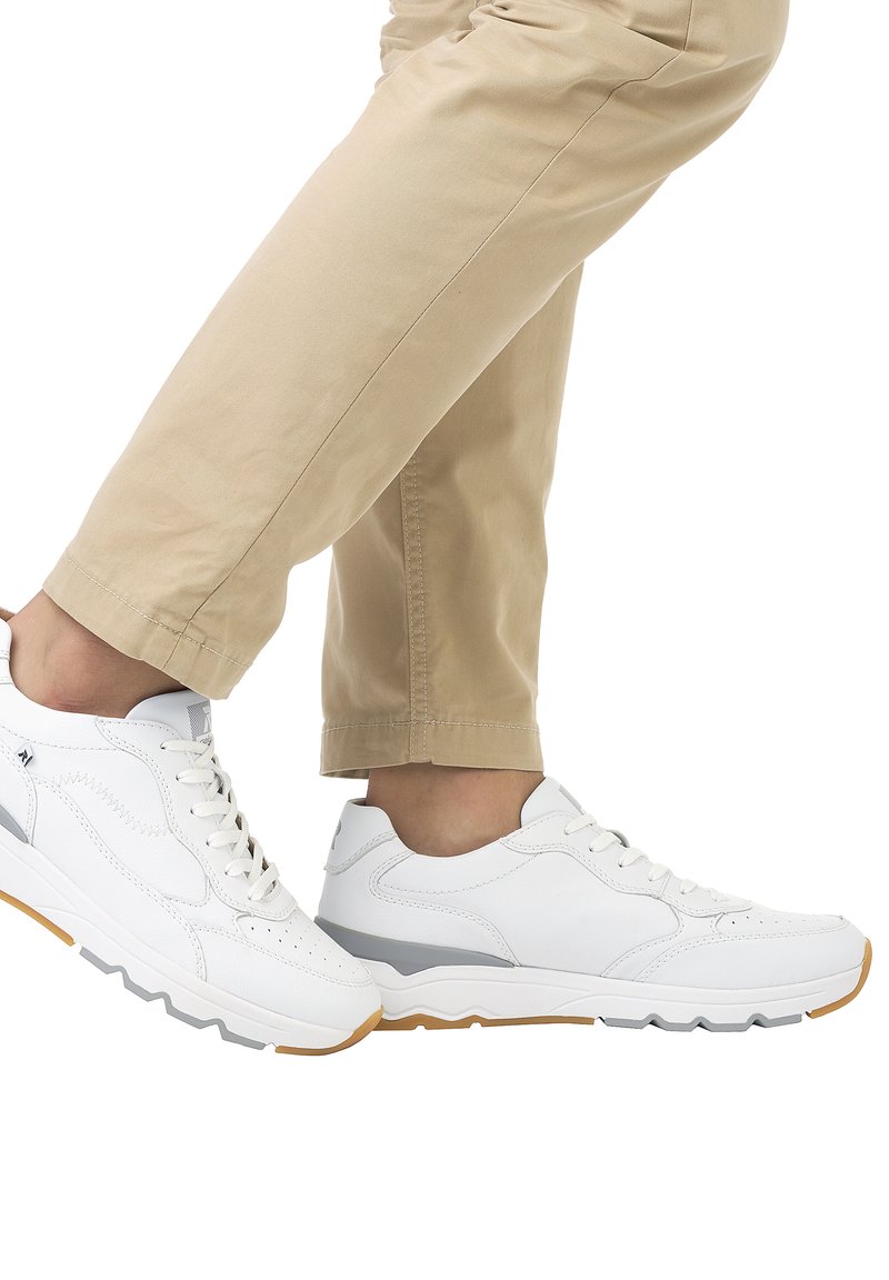 Weiße Sneakers aus strukturiertem Leder, mit grauem Akzent und einer Gummisohle mit dreieckigem Profil, kombiniert mit beigen Hosen.